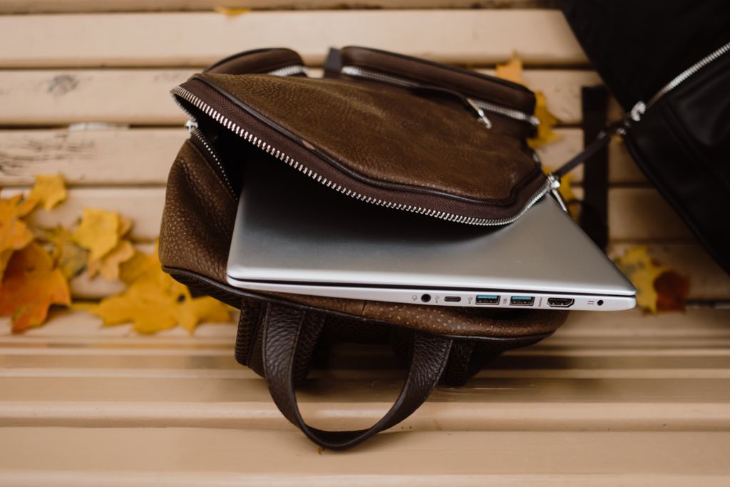 An open leather backpack with a laptop on a wooden bench surrounded by autumn leaves as the best travel backpack for laptops