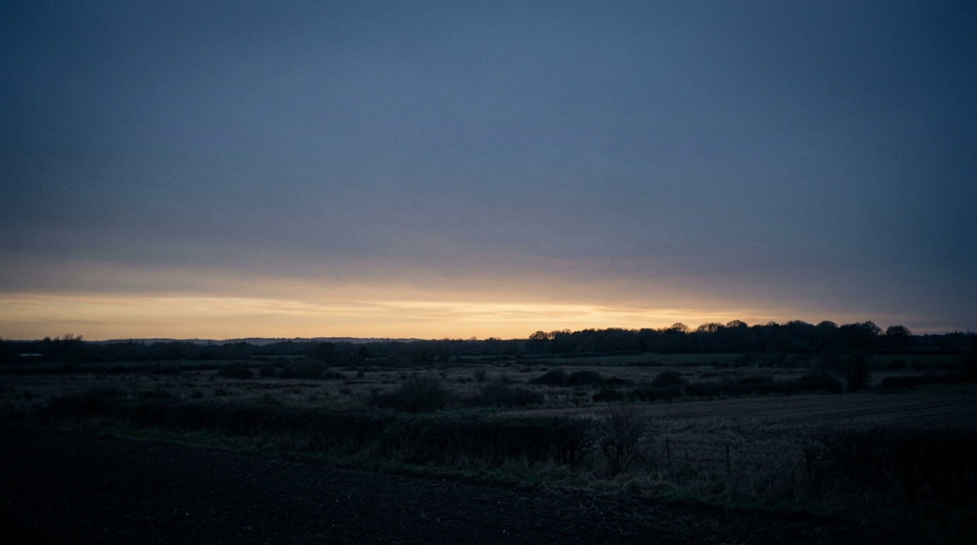 A pale gold band low on the horizon over fields already in blue shadow, the last light after sundown for sunset quotes