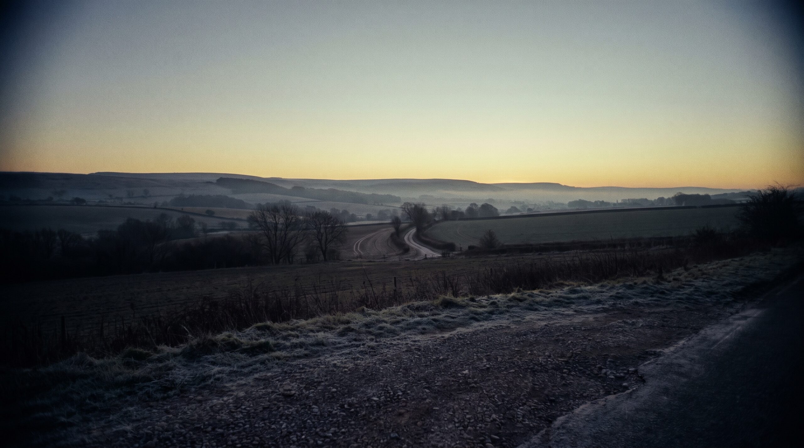 First light over open country, the sun not yet up, a pale gold band low on a cold horizon
